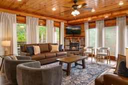 Cozy cabin-style living room with stone fireplace, TV, and wooded views