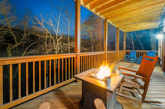 Covered deck with fire table, rocking chairs, and tranquil forest views.